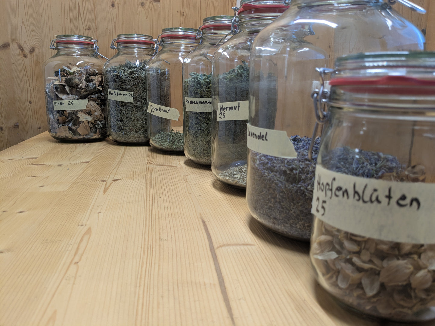 Vorratsgläser mit verschiedenen Räucherkräutern wie Lavendel und Hopfenblüten auf Holzoberfläche