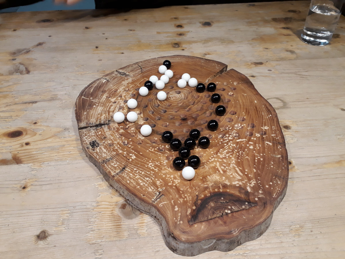 Halma Brettspiel aus Holz auf einer Baumscheibe mit schwarzen und weißen Kugeln