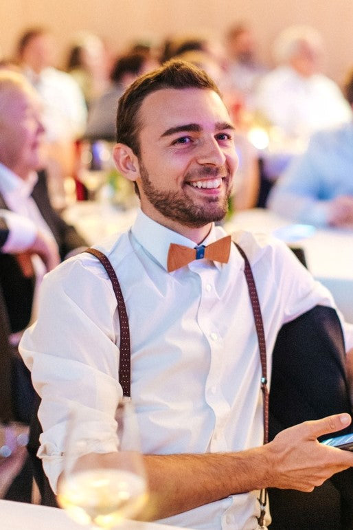 Person trägt handgefertigte Holzfliege zu Hemd und Hosenträgern bei einer Hochzeit.