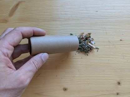 Hand hält Kartondose und schüttet getrocknete Räuchermischung Neubeginn auf hellen Holztisch.