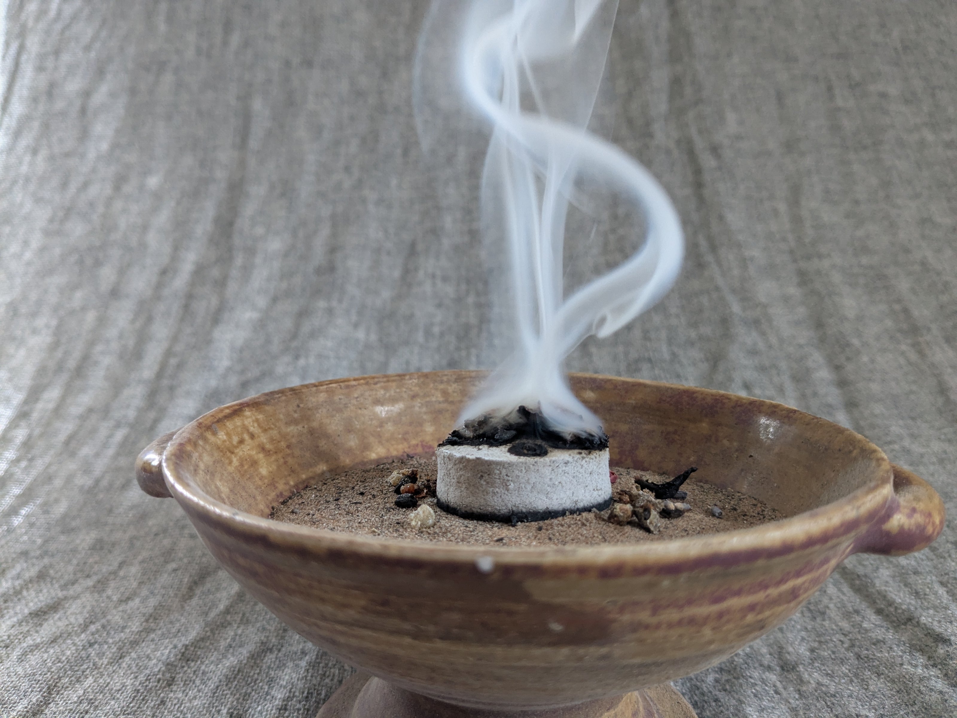 Räucherschale aus Keramik mit glimmender Kräutermischung und aufsteigendem Rauch.