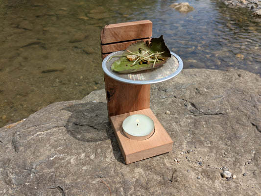 Räucherstövchen mit Kräutern auf Sieb und Teelicht in natürlicher Umgebung am Fluss.