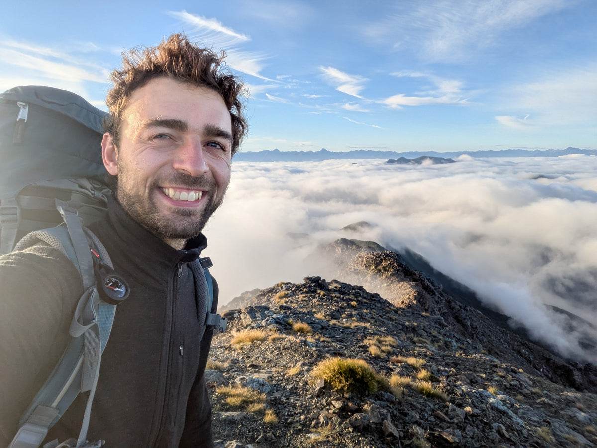 Wanderer mit großem Rucksack und Kompass auf einem Berg über den Wolken.
